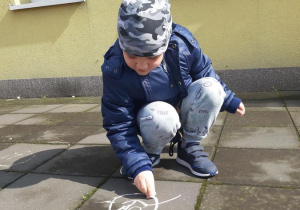 Szymek maluje kredą na chodniku.